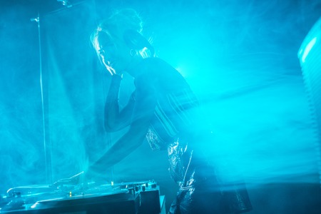 beautiful dj girl using dj equipment and smiling in nightclub with smokeの写真素材