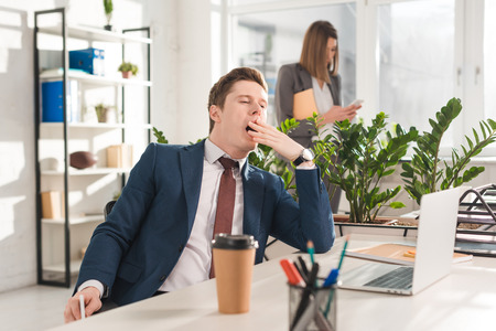 selective focus of tired businessman yawning near female coworker on backgroundの写真素材