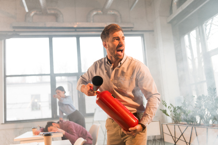 frightened businessman holding extinguisher and screaming in office with smoke near coworkersの写真素材