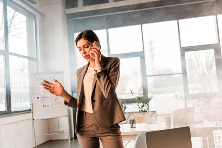 beautiful scared businesswoman talking on smartphone in office with smokeの写真素材