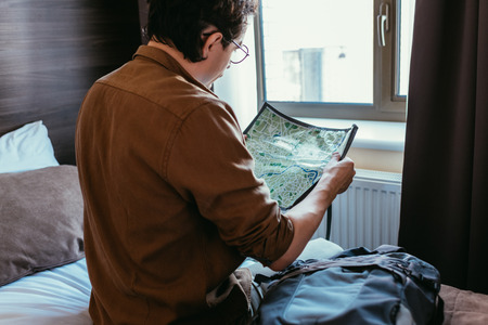 back view of male tourist looking at map in hotel room
