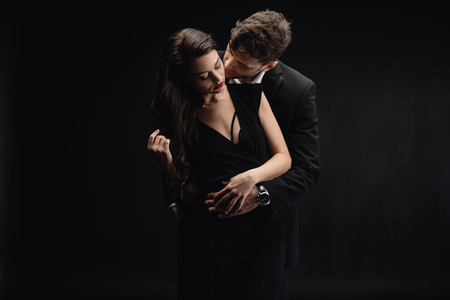 passionate young couple in formal wear kissing isolated on black