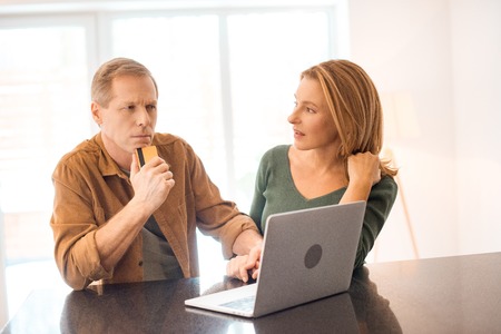 thoughtful man holding credit card while using laptop together with wifeの写真素材