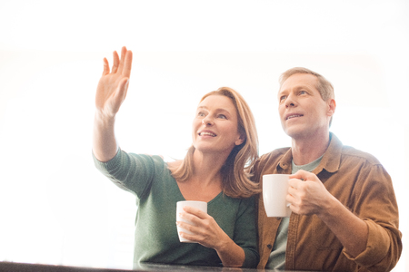 smiling woman pointing hand while standing near husbandの写真素材