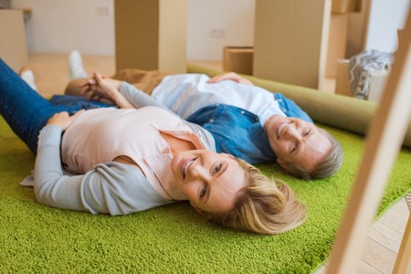 selective focus of happy couple lying on green carpet and looking at cameraの写真素材