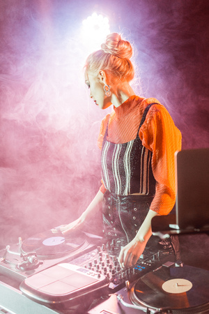 blonde dj girl touching dj equipment while standing near laptop in nightclub with smokeの写真素材