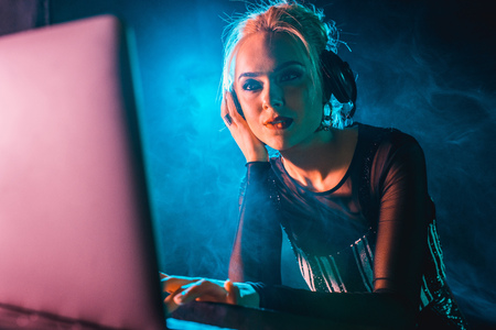 dj woman with blonde hair listening music in headphones while using laptopの写真素材