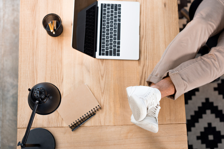 top view of laptop with blank screen near male legs in white sneakers on tableの写真素材