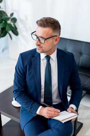 serious businessman in suit and glasses holding notebook and penの写真素材