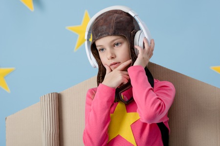 Pensive child in flight helmet listening music on blue starry background