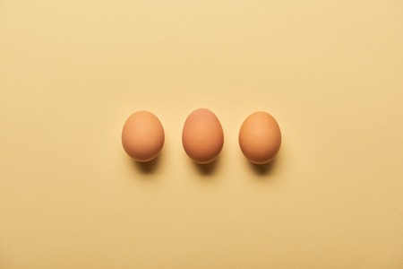 flat lay with brown organic eggs arranged in row on yellow backgroundの写真素材