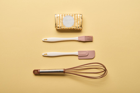flat lay with butter, balloon whisk, spatula and bakery brush on yellow background