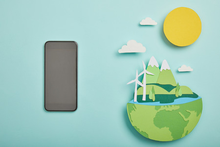 top view of blank screen smartphone and paper cut planet with renewable energy sources on turquoise background, earth day conceptの写真素材