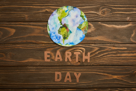 top view of paper letters and planet picture on brown wooden background, earth day concept