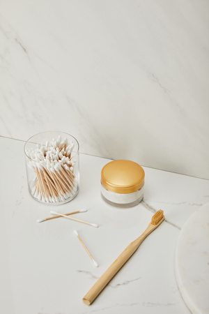 ear sticks in glass, cosmetic cream and bamboo toothbrush on white marble backgroundの写真素材