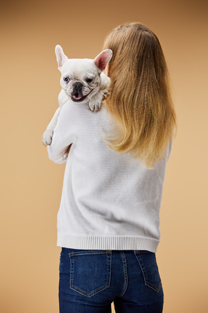 woman in white sweater and blue jeans holding on shoulder french bulldog on beige backgroundの写真素材