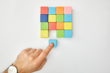 cropped view of male hand putting cube in set of multicolored blocks on grey backgroundの写真素材