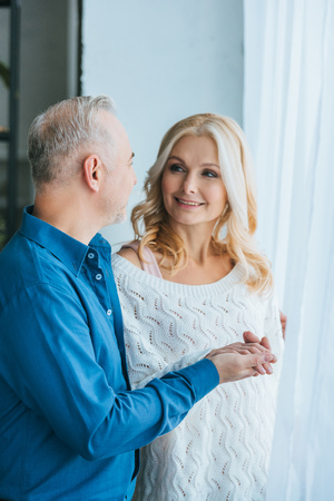 man looking at cheerful wife and holding hands at homeの写真素材