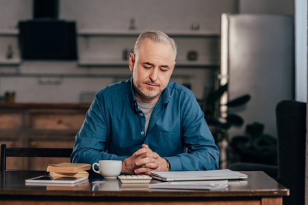 handsome man looking at cup with drink near books and digital tabletの写真素材