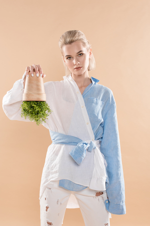 woman holding pot with plant upside down while standing in eco clothing isolated on beige, environmental saving conceptの写真素材