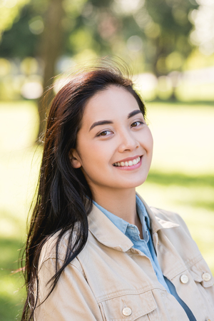 attractive young woman smiling while looking at camera in parkの写真素材