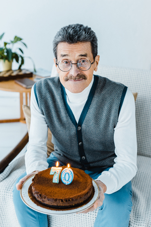 happy senior man holding birthday cake while sitting on sofa a in living roomの写真素材