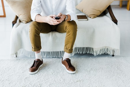 cropped view of senior man sitting on sofa and holding remote controlの写真素材