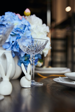 selective focus of decorative rabbits near crystal glass and flowers on wooden table at home