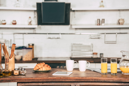 cups with drinks near glasses with orange juice and digital tablet in kitchenの写真素材
