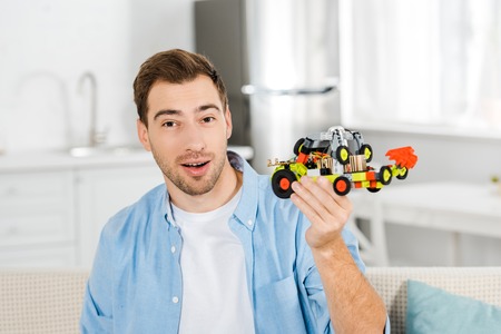 excited handsome man looking at camera and holding toy car at home