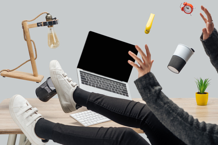 cropped view of woman levitating in air with laptop and stationery at workplace isolated on greyの写真素材