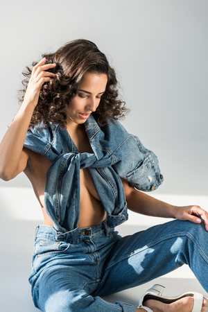 Sexy topless girl in jeans touching curly hair on grey backgroundの写真素材