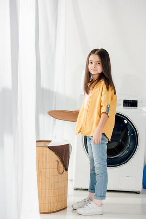 child standing near washer and holding basket cover in laundry roomの写真素材