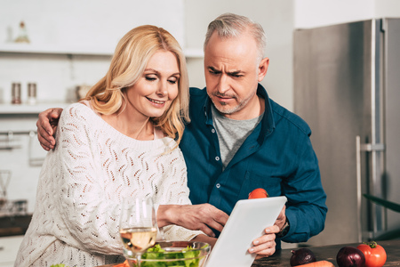 selective focus of couple looking at digital tablet in kitchenの写真素材