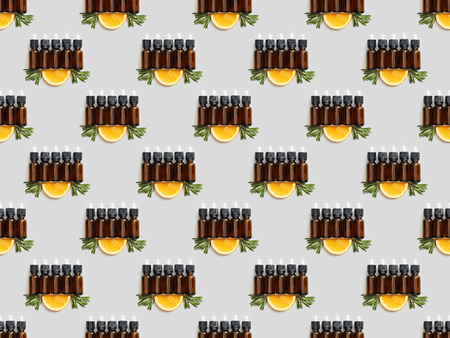 Top view of glass bottles with essential oil and orange slice on grey