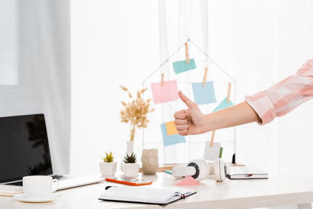 Partial view of woman showing thumb up at workplaceの写真素材