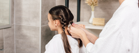panoramic shot of mother braiding daughter near shelves in bathroom