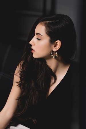 attractive brunette in elegant dress sitting on couch on black backgroundの写真素材