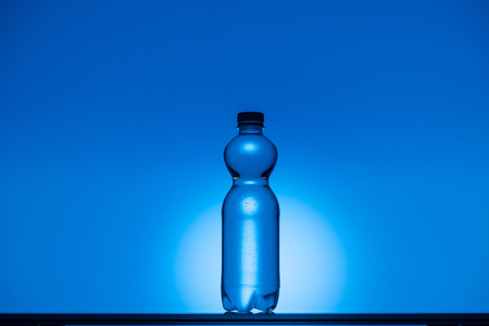 toned image of plastic water bottle on neon blue background with copy space and backlitの写真素材
