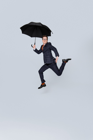 stylish businessman in suit jumping with umbrella isolated on greyの写真素材