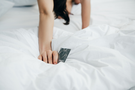 cropped view of woman holding condom on white bedの写真素材
