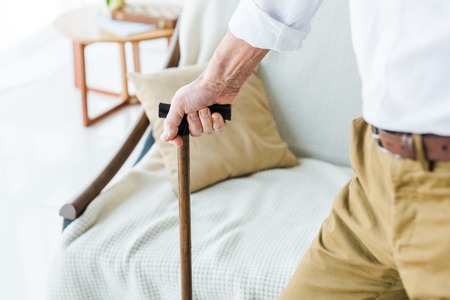 cropped view of senior man holding walking cane near sofaの写真素材