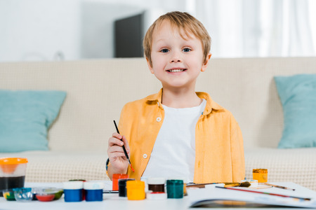 adorable smiling preschooler boy looking at camera while drawing at home