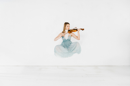 floating girl in blue dress playing violin on white backgroundの写真素材