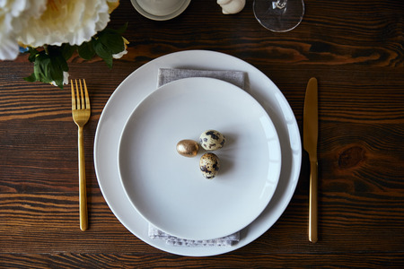 top view of quail eggs on white plates near fork and knife on wooden table