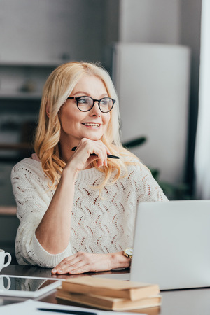 selective focus of cheerful woman in glasses sitting near laptopの写真素材