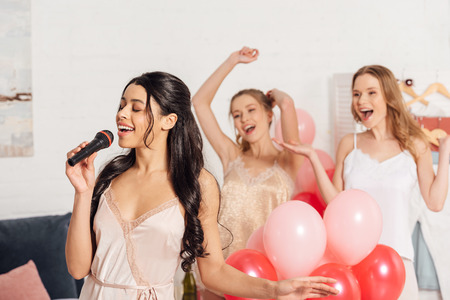 beautiful multiethnic girls in nightwear singing karaoke at pajama party in bedroomの写真素材