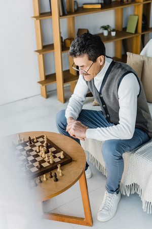 pensive retired man in glasses looking at chess board at homeの写真素材