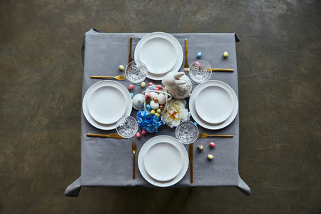 top view of table with white plates, cutlery, crystal glasses, cutlery, painted eggs and flowers at...