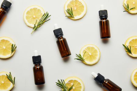 Flat lay with bottles of essential oil, lemon slices and rosemary on grey backgroundの写真素材